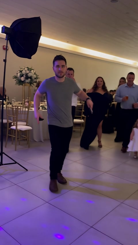 Man in a gray T-shirt taking small steps toward the camera at a banquet